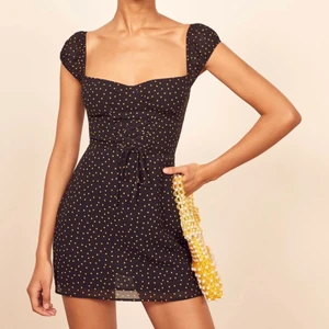 Reformation Jess dress xs/s - Supersnygg svart klänning med små gula prickar från det hållbara märket Reformation. Klänningen har en hjärtformad ringning, öppen rygg med smock och snygg dekorativ knytning framtill. Klänningen är storlek 6 vilket motsvarar 36 eller xs/s. Enbart använd vid två tillfällen då den tyvärr är lite för liten för mig. Inköpt från deras egen hemsida 2019. 