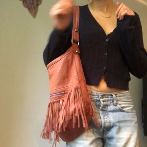Handväska - Häftig handväska som blir perfekt till hösten! Den är lite sliten och har lite fläckar på insidan. Annars funkar den hur bra som helst! Rosa tyg på insidan och coola fransar i läder på utsidan. 