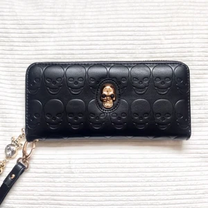 Plånbok/Clutch - Svart plånbok/clutch med dödskalledetaljer. Kan också användas som en clutch med den avtagbara remen. Guldiga detaljer. Läderimitation. Perfekt skick (använd 1-2 gånger).