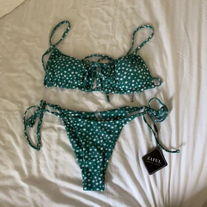 Jessica Stockstill X ZAFUL Ditsy Print Cutout String Bikini Swimwear - Green S - Fin oanvänd grön-vit blommig bikini. Lappen och plasten är fortfarande kvar. Knytbar underdel i sidorna och även överdelen knyts både i ryggen och fram. Den sitter bra och man kan justera så den passar sin kropp men tyvärr lite stor för mig. Ordinarie pris: 26,90 €. Hör av er om ni undrar något