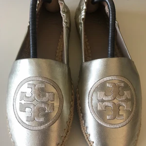 Tory Burch skinn espadrillos i stl 37 nyskick!!! - Grymt snygga espadrillos från lyx märket Tory Burch i stl 37. Guld färgad med skinn runt om hela skon. Butikspriset var 1800kr och är i nyskick. Endast under sulan har lite skrap. Kan buda om fler är intresserade med 10kr+. Köparen står för spårbar frakt med PostNord 66kr. Kan mötas upp också.