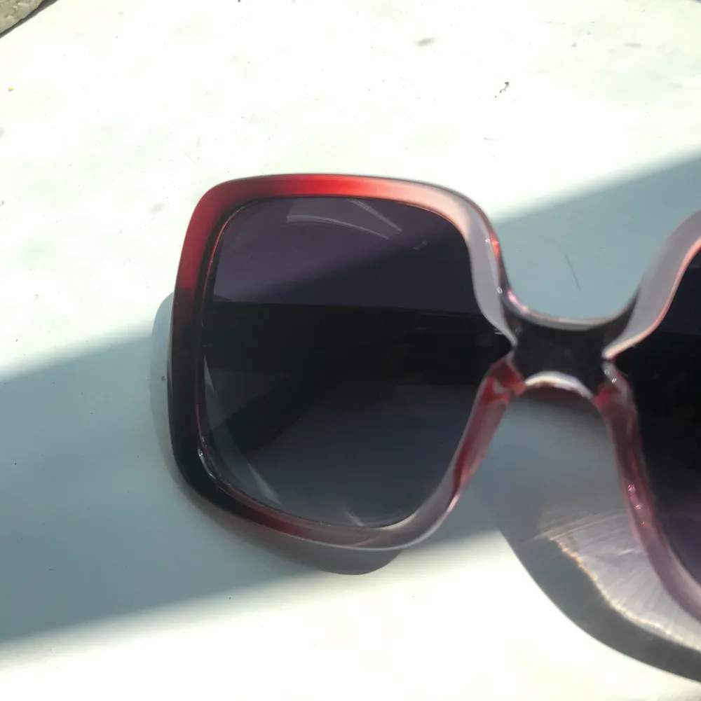 Stora fyrkantiga solglasögon som skiftar i rött rosa och genomskinligt. Accessoarer.