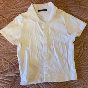 Vit croppad t-shirt från ”brandy Melville” med knappar och en liten krage. Använd en gång. Säljer den för att den var lite för liten för mig. Storlek XS/S. (Du betalar priset+frakt)