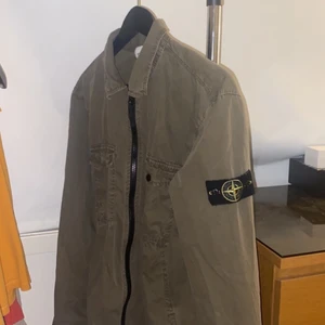 Stone island overshirt storlek M - Denna stone island overshirt är i en grön/brun unik och cool färg och passar M men är lite oversized skulle säga att skicket på den är 8-9 av 10. OBS KÖPAREN STÅR FÖR FRAKT.