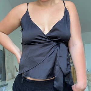 Nelly.se - Svart glansigt linne med tunna band och knyte i midjan! 