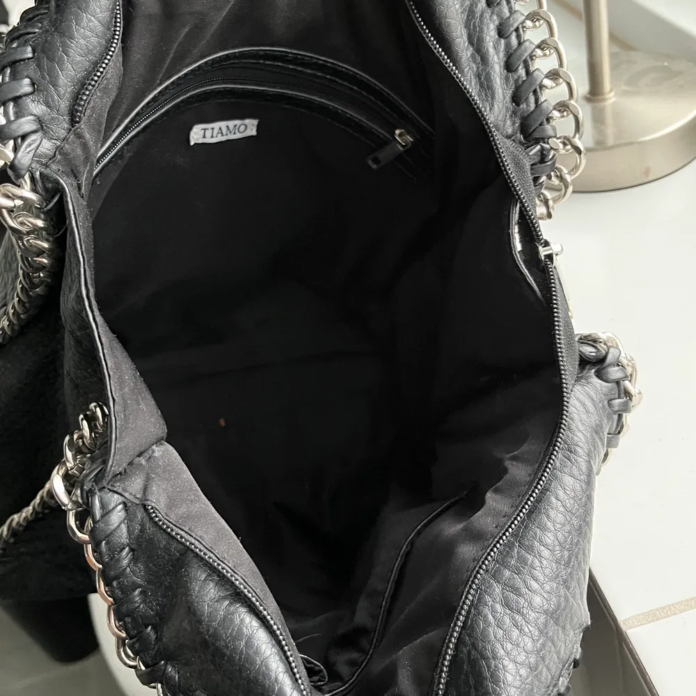 En svart väska i läderimitation som har silvriga detaljer. Den är använd men inte sönder. Fler bilder kommer på skicket idag, har inte tillgång till väskan just nu! . Väskor.
