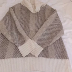 Mönstrad stickad polotröja  - Oversized stickad tröja med mönster i beiga toner. Kragen är hyfsat lång men går vika ner.