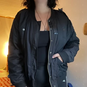 Bomberjacka - Svart bomberjacka med rött foder. Storlek 44, uppskattar den till stor L/XL. Har armficka med dragkedja. Använd men i gott skick. Säljes pga för stor. !! Fläcken på sista bilden är på kameran, inte jackan. 💌Frakten är baserad på frimärken. Önskas postnords egna paket löser vi det. 🎈