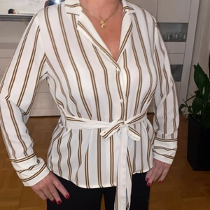 Skjorta från gina strl 38 - Superfin randig skjorta fast inte i ”skjortmaterial”. Vilket gör att den inte blir skrynklig! Finns ett band som man kan knyta en rosett om man vill. Det kan mna göra på sidan eller i mitten.