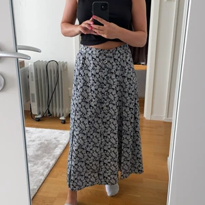 Mörkblå långkjol - En mörkblå långkjol i en mörkblå färg med ett vit mönster. Kjolen är knappt använd och i väldigt bra skick (en knapp längst ner har gått av men inget som märks). Oklart vad för stolek det är men kjolen passar mig som vanligtvis bär s/m. 