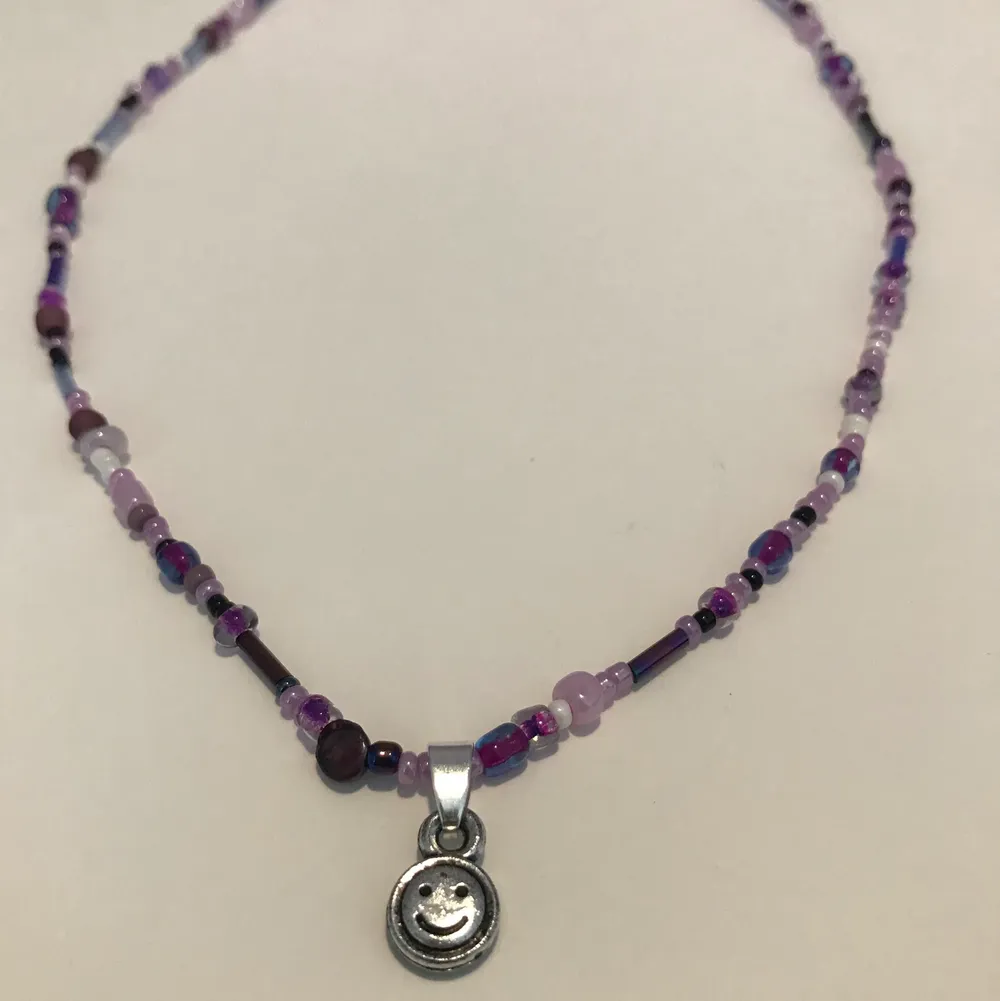 Ett gulligt halsband i olika lila nyanser med en silvrig  smiley😊 . Accessoarer.