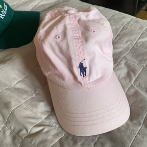 Ralph Lauren keps - Använd men ok skick! Går säkert att tvätta också. Superfin ljusrosa färg med mörkblå häst.