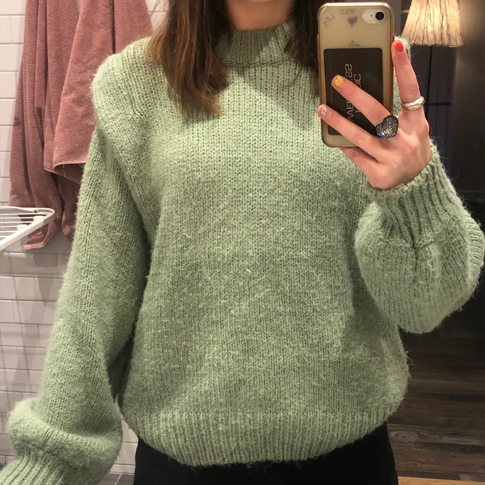 Detta är en grön stickad tröja som är köpt på Gina tricot. Den är oversized i modellen och har superfina volanger vid armen. Stickat.