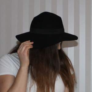 Trendig svart hatt i 100% ull. Band runtom (bild 3), onesize.