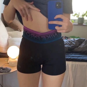 Nike PRO shorts - Svarta Nike PRO shorts med hög midja. Midjan är blå som skiftar över i lila och resten av shortsen svarta. Materialet i midjan är luftande och skönt samtidigt som det sitter på plats. Köpta sommaren 2020 och sparsamt använda. 200kr+frakt.