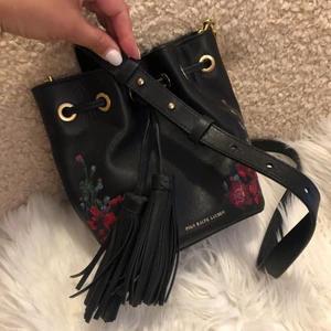 Superfin sommarväska Ralph Lauren - Så söt liten Ralph Lauren väska med tofsar och broderade blommor på svart skinn. Rymmer mobilen o liten sminkväska. Köpt på NK