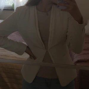 En kavaj i vitt/beige färg i storlek 34 från H&M. Använd ett par gånger. Väldigt skönt material. Har en kanpp i mitten  - Passar storlek 34 