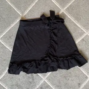 En fin svart omlott kjol från Gina Tricot med volangkanter och rosettknytning, storlek M
