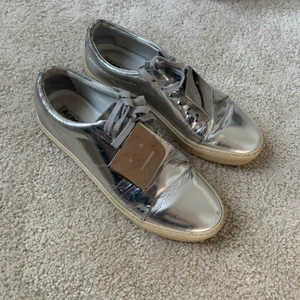 Acne Studios Adriana sneakers (metallic silver) strl 38 - Acne Studios sneakers i modell Adriana (metallic silver) storlek 38. Ganska använda med lite slitage baktill (se bild), annars finfina.  Nypris ca 3000 kr.  500 kr eller högst bjudande. Skorna kan skickas, fraktkostnad tillkommer.