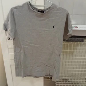 Ralph lauren polo - En polo tröja. I bra skick men har dock ett litet hål på ryggen visar på andra bilden. Den är grå med ett märke på vänstra bröstet i färgen svart/blå. Original pris 200kr men säljer för 120kr