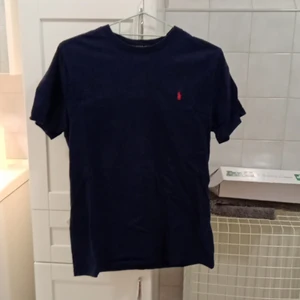 Ralph Lauren polo - En polo tröja. Den är i bra skick med inga fläckar eller håll. Den är blå/svart med ett rött märke på vänstra bröstet. Säler pågrund av att den aldrig används. Original pris 200kr men säljer för 120kr