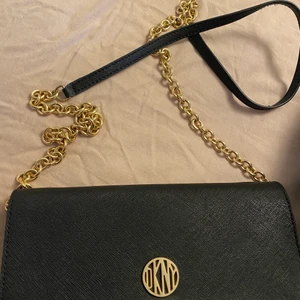 DKNY väska - En äkta DKNY väska köpt i USA på en DKNY butik, väskan är i väldigt bra skick och knappast andvänd. Det går även att andvända den som en plånbok då kedjan går att ta bort 