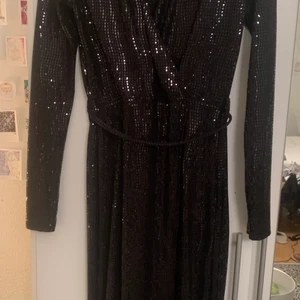 Svart omlottklänning med paljetter, S - Glittrig omlottklänning från Gina Tricot. Endast använd en gång. Sitter tight med djup urringning och slits. Storlek S. 