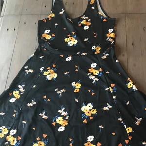 Svart blommig klänning  - En svart klänning med blommor på och låg rygg. Köparen står för frakten 