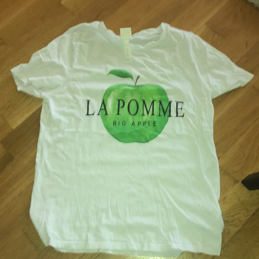 En vit t-shorts med ett grönt äpple och texten:            (la pomme). T-shirts.