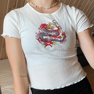 Topp med motiv - Topp med broderad drake framtill o storlek S. Aldrig använd så i nyskick. Hör av er vid frågor eller om ni vill ha fler bilder💞