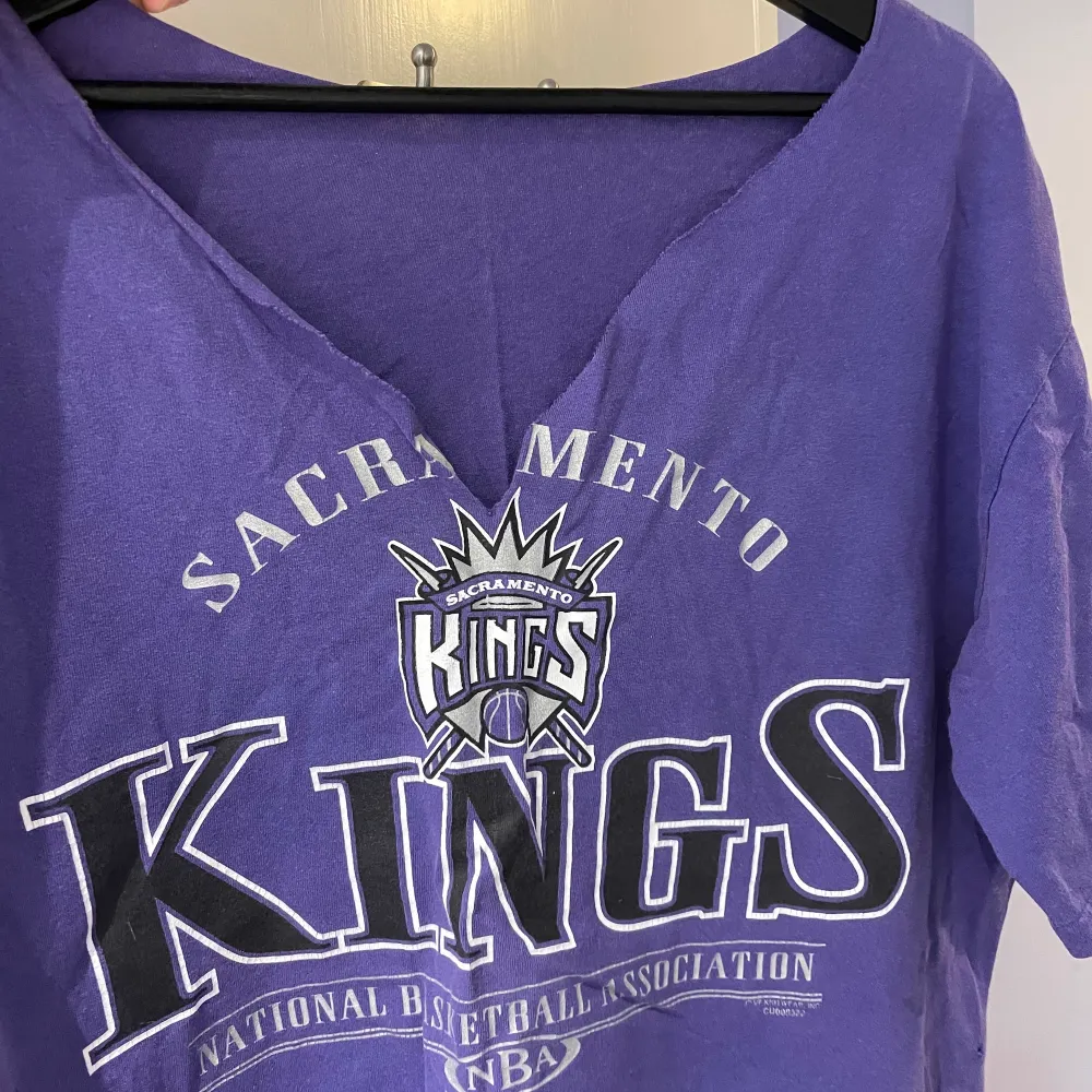 Retro baskettisha med ”KINGS” på. Kragen runt halsen är avklippt, samt en slits klippta på varje sida av tishan (se bild två). . T-shirts.