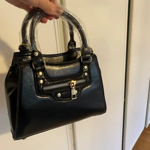 Svart handväska  - Jätte söt handväska med guld detaljer. Aldrig använd därav plasten kvar. Det ingår även ett längre band till väskan! Kan mötas i Sthlm annars står köparen för frakten😆😆