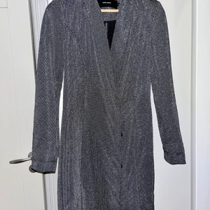 Kavajklänning - Diskret glittrig kavaj som är som en klänning. Är 167 cm och den täcker låren på mig. Dubbel knäppning och lite vadderad vid axlarna! Magisk passform! Stretchiga material. Perfekt till nyår! 