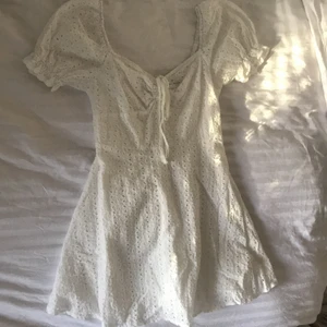 Vit student/skolavslutnings klänning - Säljer nu min studentklänning som man även kan ha till skolavslutning eller sommar. Endast använd 1 gång, inga fläckar eller något som är sönder. Storlek M men passar även S. Kvadratisk skurning och man kan justera hur mycket man vill visa genom att dra åt rosetten. Har dragkedja i bak. Vit spets🥰