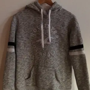 Hollister Los Angeles Hoodie. Grå i skiftande nyanser med 2 band runt armen och logga på bröstet. Jätteskönt material på insida, som kan ses på andra bilden. Plagget är använt ett antal gånger men absolut inte i dåligt skick 