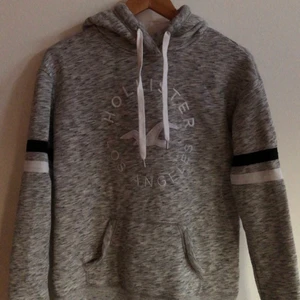 Hollister hoodie  - Hollister Los Angeles Hoodie. Grå i skiftande nyanser med 2 band runt armen och logga på bröstet. Jätteskönt material på insida, som kan ses på andra bilden. Plagget är använt ett antal gånger men absolut inte i dåligt skick 