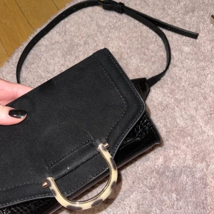 Svart midjeväska - Svart midjeväska som man kan ha runt midjan eller över bröstet. Coola detaljer och väldigt modern 