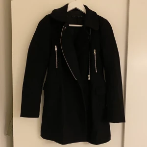 Svart kappa med avtagbar pälskrage - Svart jättesnygg halvlång kappa från Zara. Avtagbar pälskrage i fake-päls. Snygg både knäppt och öppen. Storlek XS.