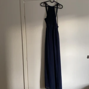 Balklänning  - Marinblå balklänning med slits. Strass detaljer på banden på ryggen. Dragkedja på sidan av klänningen. Använd vid 2 tillfällen. Inget slitage, klänningen är i nyskick. Perfekt klänning till bal eller fina tillställningar.