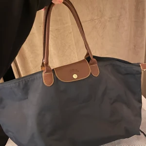 Longchamp väska  - Väskan är fin och har hållit sitt skick. Har defekter som man kan se på bilderna, det finns ingen dragkedja och vid ett av banden har sömnen gått upp lite grann. Annars är den rymlig och är ca 40-50 cm lång.
