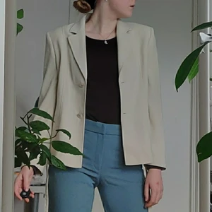 Beige kavaj med knytband - Beige kavaj från det mexikanska klädmärket Ivonne med tillhörande knytband/skärp. Storlek 8/38, och passar upp till M (lite oversize). Egenskaper och detaljer: beige, 2-knapps knäppning, knytband, axelvaddar Märke: Ivonne Material/komposition: 100% polyester och 100% acetat Skick: begagnad men i bra skick 