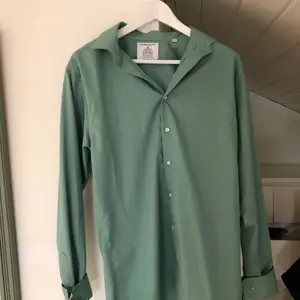 En grön skjorta från ”The Shirt Factory” i mycket bra skick då den endast är använd ett fåtal gånger. Det är en herrskjorta i storlek 40, nypris ligger på ungefär 1000 kr.