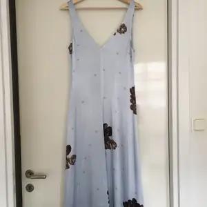 Superfin klänning från ganni i ljusblått silkesmaterial med bruna blommor. A-linjeformad modell, i storlek 36. Helt oanvänd, med prislapp fortfarande på.
