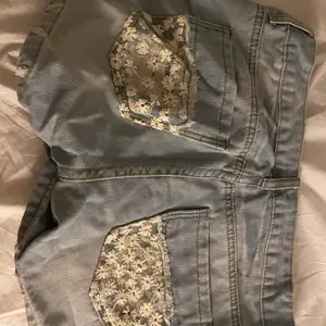 Jeans shorts med blommiga spets detaljer på fickorna.  