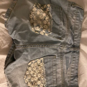 Jeans shorts strl L - Jeans shorts med blommiga spets detaljer på fickorna.  