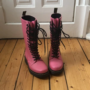 Rosa gummistövlar (Dr.Martens) - Ett par fantastiskt söta, rosa gummistövlar med svart snörning från Dr.Martens. Köpta second hand, men knappt använda av mig, så de är i väldigt fint skick förutom lite smuts som knappt syns. Kan skicka närbilder om så önskas! Säljes pga en dåraktig bedömning att jag skulle orka klämma in mina 38-fötter i ett par 37or.