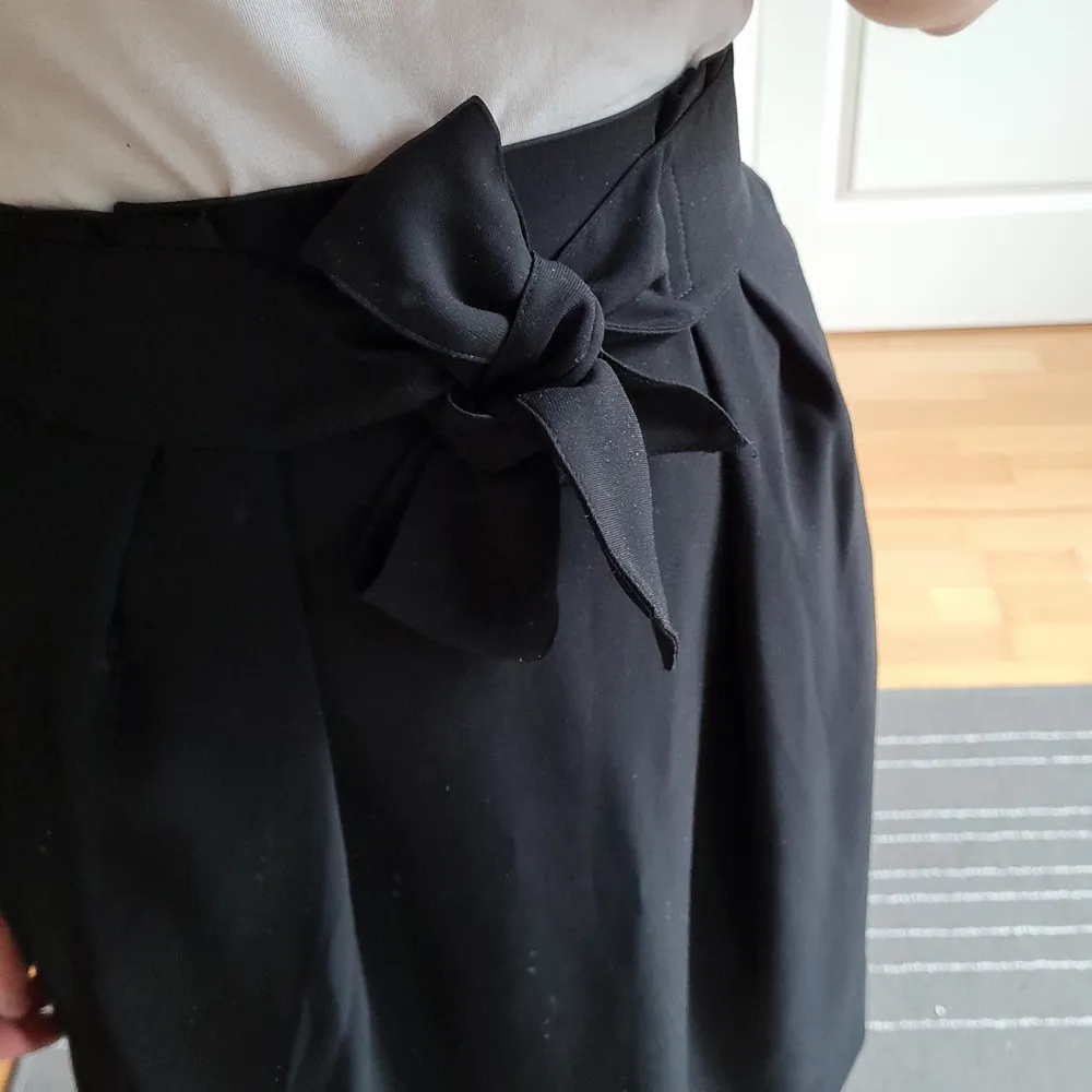 Black short skirt with zipper and button fastening from H&M. Classic looks makes it great for every occasion. Flowy fabric, cute bow in front 🥰 Used only once. Waist 36 cm, total length 54 cm.. Kjolar.