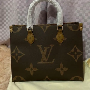 Lv äkta  - Louis Vuitton, "Onthego GM", väska  Väska i monogram samt monogram reverse canvas med detaljer i guldfärgad metall. Invändigt fodrad i rött tyg. Tre innerfickor, en dragkedsförsedd. Märkt "LOUIS VUITTON PARIS made in France" samt date code. Dustbag samt Ask  Ca 41 cm x 33 cm x 17 cm