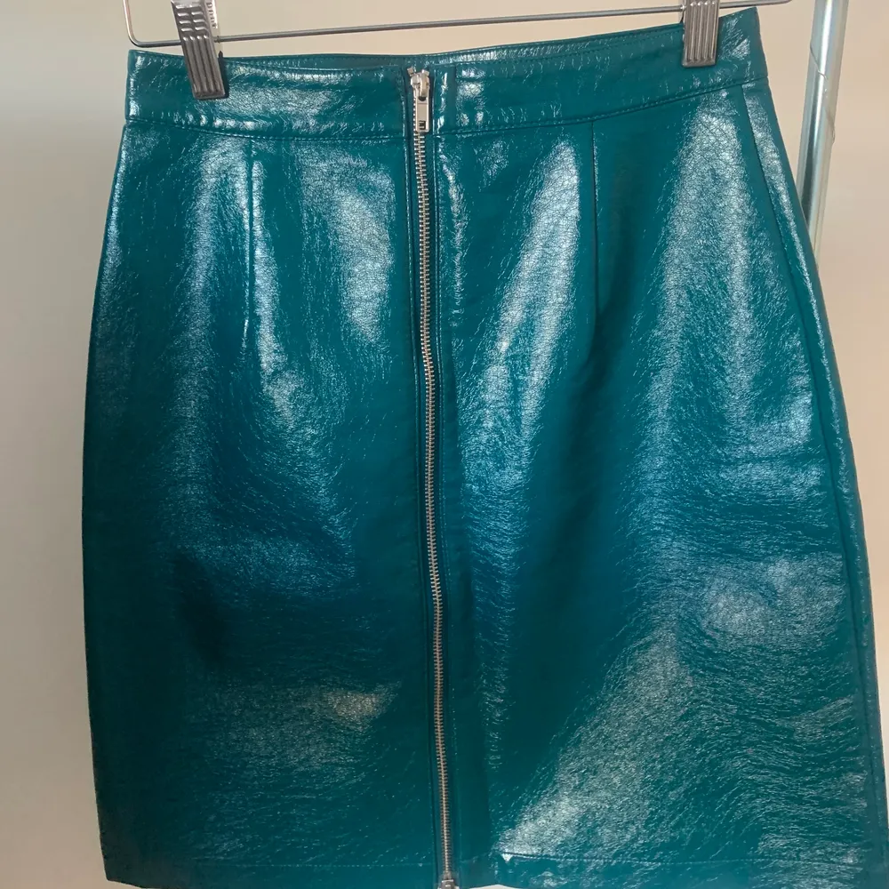 Faux leather A-line skirt in a beautiful petrol green colour (on the pictures the skirt appears more blue than in real life). There is a zipper in the back. The skirt is highwaisted and fits to mid-thighs. It is fitted on me, but can also be less fitted on someone of a smaller size than me. The skirt has never been worn before so it is in perfect condition. . Kjolar.