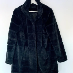 Svart pälsjacka i nyskick/ storlek 40/ hög krage - Fuskpäls med hög krage. Dold knäppning med hakar och två infällda fickor. Mjuk och följsam kvalitet med blankt, vävt foder. Längd ca 84 cm i stl 38. 100 % polyester. Använd två gånger, i nyskick! Mycket bekväm. Säljes då jag rensar i garderoben. :)